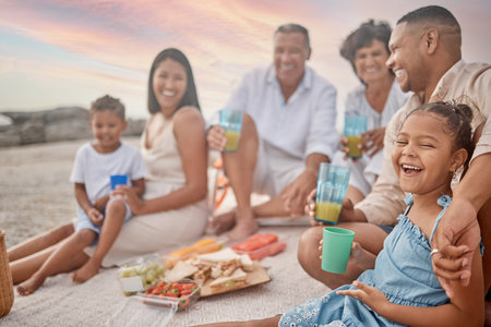 Closeup of a mixed race family having a picnic on the beach and smiling while having some food with snacks. Happy family bonding on a day out at the beachの写真素材