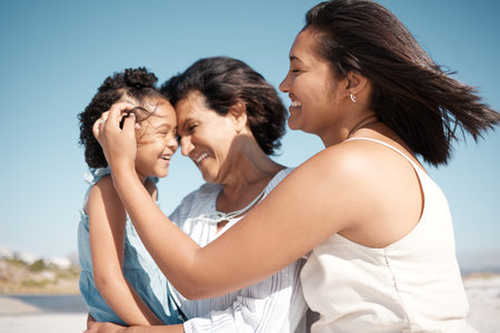 Smiling mixed race family standing together on a beach. Happy hispanic grandmother bonding with granddaughter over a weekend. Adorable little girl enjoying free time with single mother and parentの写真素材