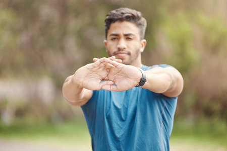 Closeup of hands of one fit young indian man stretching arms for warmup to prevent injury while exercising outdoors. Male athlete preparing body and muscles for training workout or run at the parkの写真素材