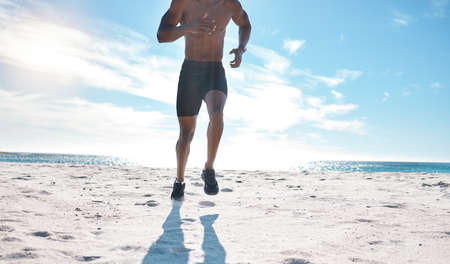 Fit young black man running and jogging at the beach in the morning while exercising. Closeup of one...