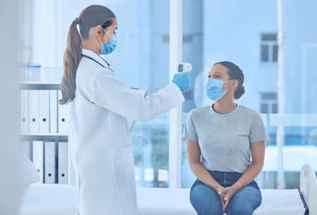 Patient having her temperature checked with a thermometer. Doctor in a clinic using a thermometer to...