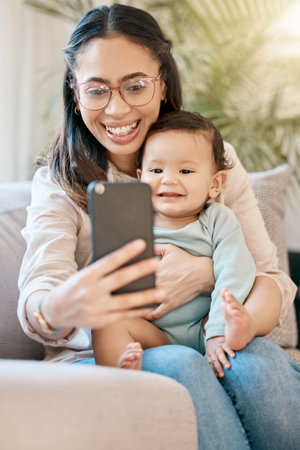 Lets call dad to say hi. a woman looking at her cellphone while sitting with her baby on her lap.