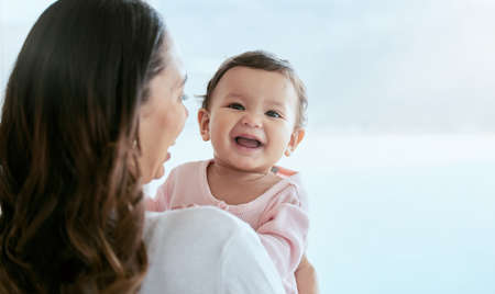 Just saying hello. a mother holding her baby daughter at home.の写真素材