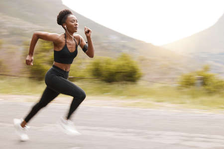 One african american female athlete looking focused while out for run to increase her cardio and endurance. A young black woman running outside to increase her speed and pace. Fitness is a lifestyleの写真素材