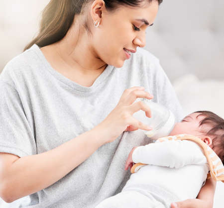 Young hispanic mother feeding her newborn baby a milk bottle and bonding with her. Little baby...