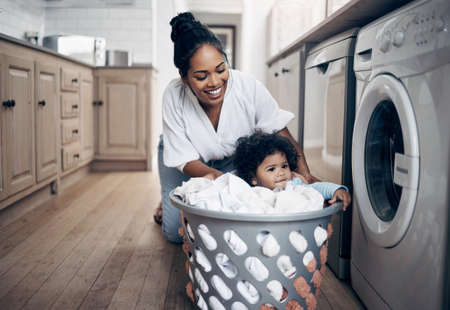 Who needs a nanny. a young mother playfully bonding with her baby girl while doing the laundry at home.の写真素材