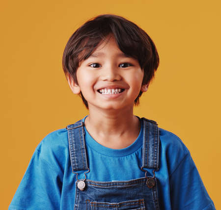 Portrait of a cute little asian boy wearing casual clothes while smiling and looking excited. Child standing against an orange studio background. Adorable happy little boy safe and aloneの写真素材