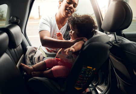 Doing it all by herself. a young woman strapping her baby into her car seat.