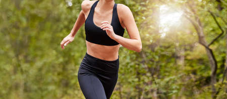 Close up of a womans fit body wearing workout clothes while out for a run at a park or in nature on a sunny day. Woman exercising and living a healthy lifestyleの写真素材