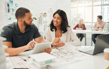 Coworkers talking about building blueprint. Young designers planning a building project. Two...