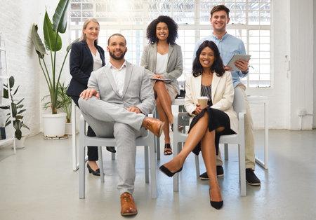 Portrait of a group of five cheerful diverse businesspeople sitting together at work. Business professionals having a meeting in an office. Colleagues planning togetherの写真素材