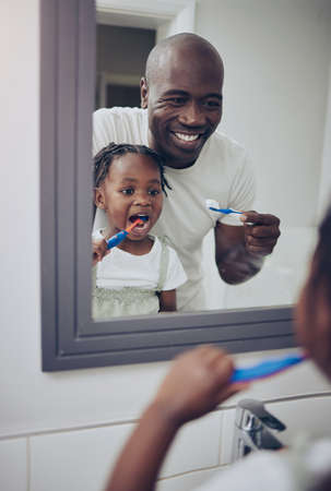 Take your time when you brush. a little girl and her father brushing their teeth at home.の写真素材