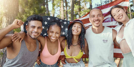 Happy 4th of July. a diverse group of friends standing and holding the American flag during a day in the woods.の写真素材
