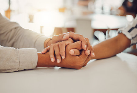 Close up of young man and woman holding hands at wooden table, from above. Loving couple expressing...