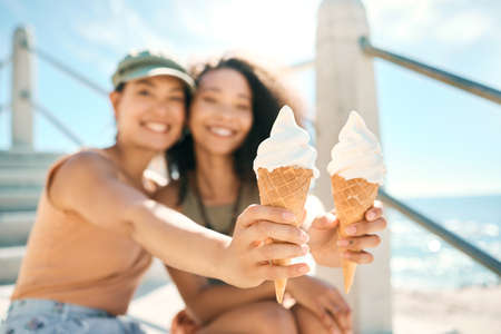 To a fun-filled summer. Cropped portrait of two attractive young girlfriends enjoying ice creams on the beach.の写真素材