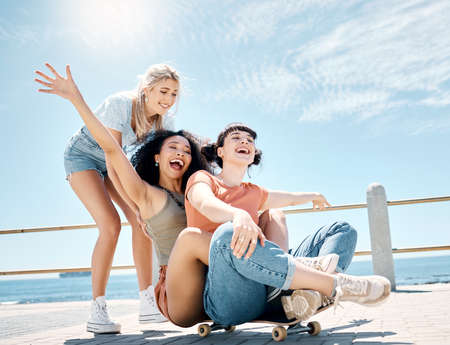Learn to live a little. Full length shot of a diverse group of women bonding while playing with a skateboard outdoors.の写真素材