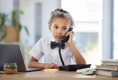 Ive been on hold for hours. an adorable little girl dressed as a businessperson sitting in an office and using a telephone.の写真素材