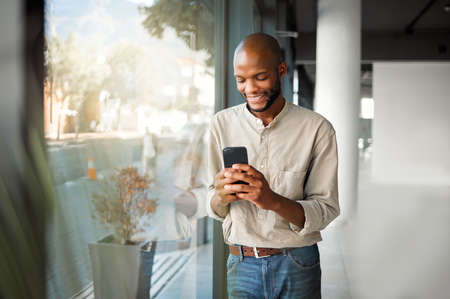 Cheerful african american businessman typing a message on a phone at work. Happy male business...