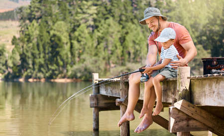 Well be reeling in a little fishy soon. a little boy fishing with his father at a lake in a forest.の写真素材