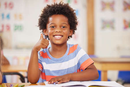 A curious mind builds a strong character. a preschool student showing thumbs up while sitting in...
