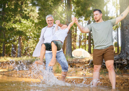 Up, up and away. a little boy having fun with his father and grandfather at a lake in a forest.の写真素材