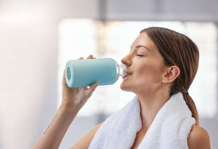 One fit young caucasian woman taking a rest break to drink water from bottle while exercising in a...