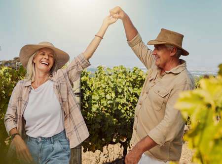 Smiling senior couple dancing together and feeling playful on vineyard. Caucasian husband and wife standing together and enjoying a day on a farm after wine tasting weekend. Man and woman having funの写真素材