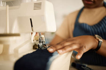 Closeup of hands of tailor using sewing machine. Fashion designer feeding denim through sewing...