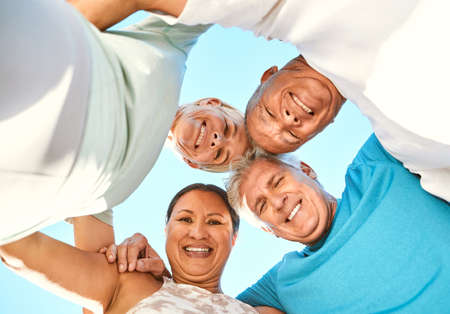 Below portrait view of a group of senior friends standing together in a huddle. Smiling active...