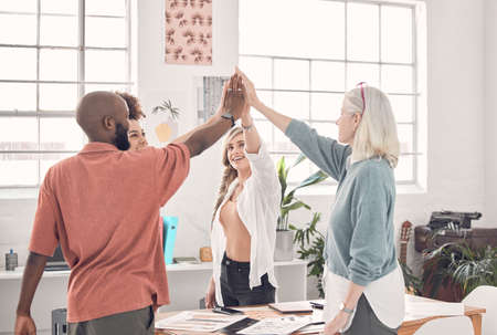 Group of diverse businesspeople giving each other a high five in an office at work. Business...