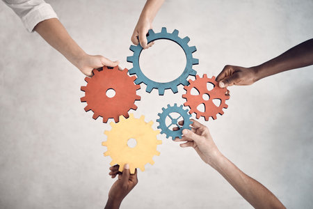 Group of five businesspeople holding and fitting gears together in an office at work. United...