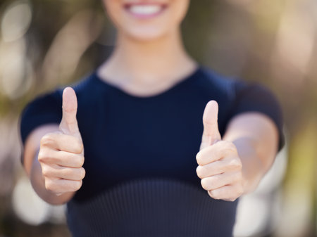 Close up of female hands showing thumbs up. Young female athlete gesturing with her hands while out for a workout. Sportswoman enjoying exercise outdoorsの写真素材