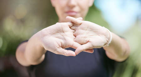 Close up of female athlete interlocked hands while stretching her arms during workout in nature on a sunny day. Fit sportswoman doing warmup exercise before her run in natureの写真素材