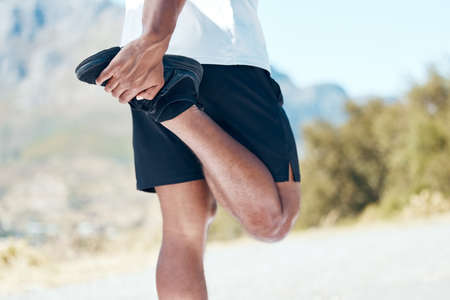 Closeup of an unknown man standing alone and stretching during his outdoor workout. Fit male warming up before a run outsideの写真素材