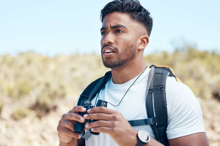 Closeup of a mixed race male using a binocular during a hike outside. Young handsome indian male looking at a view while out on a walk in natureの写真素材