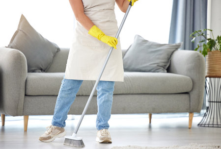 An unrecognizable woman cleaning the floor of her apartment. One unknown woman using a broom to clean the floor of dustの写真素材
