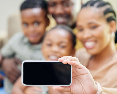 Say cheese. an unrecognisable family sitting on the sofa together at home and taking selfies on a cellphone.の写真素材