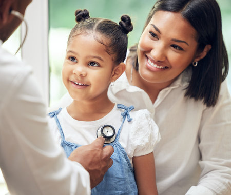 Doctor examining happy little girl by stethoscope. Child sitting with mother while male paediatrician listen to chest heartbeat. Mom holding daughter during doctor visitの写真素材