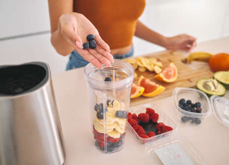 This is going to be berry delicious. a woman putting a variety of fruits into a blender at home.の写真素材