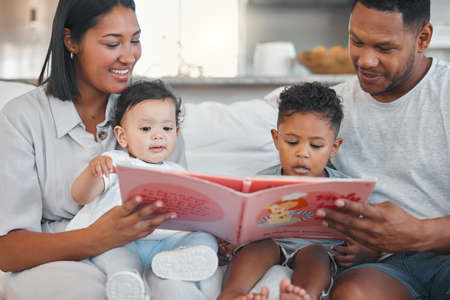 Never too young for story time. a young family happily bonding together while reading a book on the sofa at home.の写真素材