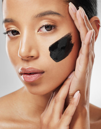 Keep calm and mask on. Studio portrait of an attractive young woman wearing some charcoal face mask against a grey background.の写真素材
