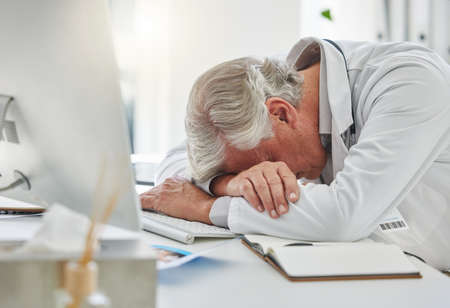 Getting a quick nap in. a mature doctor sleeping at his desk at work.の写真素材