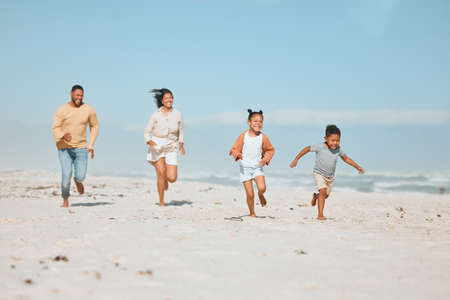 Cheerful young mixed race family running on the beach, Happy mother and father with two children having fun during summer holiday. Playful casual family racing on sandy beach enjoying time togetherの写真素材