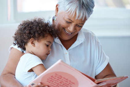 A story before bedtime. a mature grandmother reading her granddaughter a story at home.の写真素材