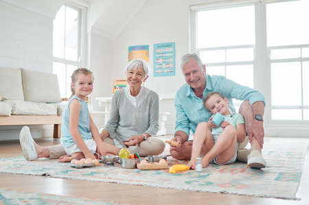 Our grandparents house is like our second home. two little girls playing with their toys while sitting at home with their grandparents.の写真素材