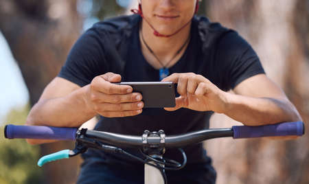 One athletic unrecognizable male using a cellphone while cycling outside on a bike for exercise....
