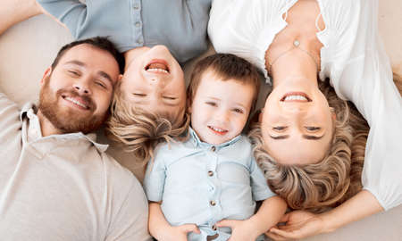 Portrait of smiling caucasian family of four from above lying and relaxing on floor at home. Faces of carefree loving parents bonding with sons. Young boys spending quality time with mom and dadの写真素材