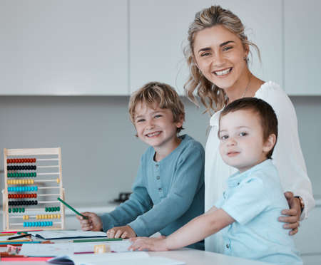 Portrait of a young happy caucasian mother helping her sons with homework at home. Carefree siblings smiling having fun and drawing with their mom. Brothers doing schoolwork with the help of momの写真素材