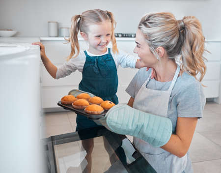Mother and daughter removing tray of muffins from the oven. Happy woman baking muffins with her...