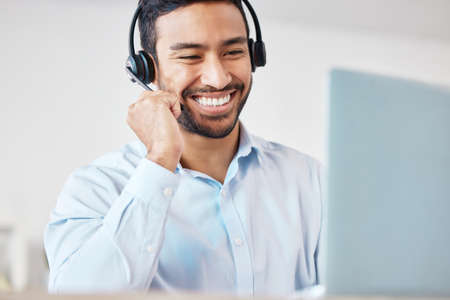 Smiling mixed race male call centre agent smiling while wearing a wireless headset. Young man...
